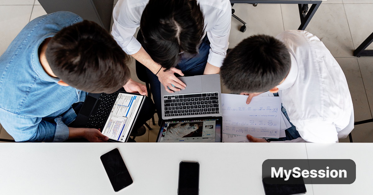 Three colleagues working together around laptops and documents at a shared office desk